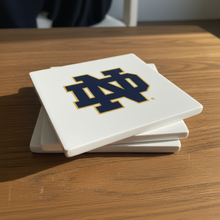 Load image into Gallery viewer, Stack of stone coasters with a logo on a wooden surface