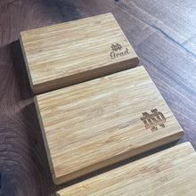 Load image into Gallery viewer, Three wooden cheese boards with Notre Dame branding on a wooden surface