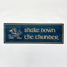 Load image into Gallery viewer, This Shake Down the Thunder wall art is laser cut and engraved and features a blue or green stained background with birch wood letters, accents and the Notre Dame Leprechaun. The art is 30" x 10" to make it perfect for your dorm room, apartment, or home!