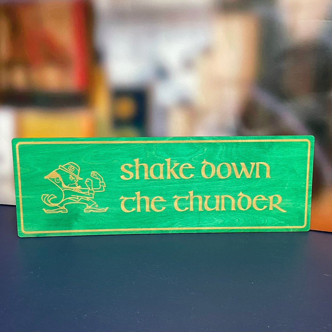 This Shake Down the Thunder wall art is laser cut and engraved and features a blue or green stained background with birch wood letters, accents and the Notre Dame Leprechaun. The art is 30